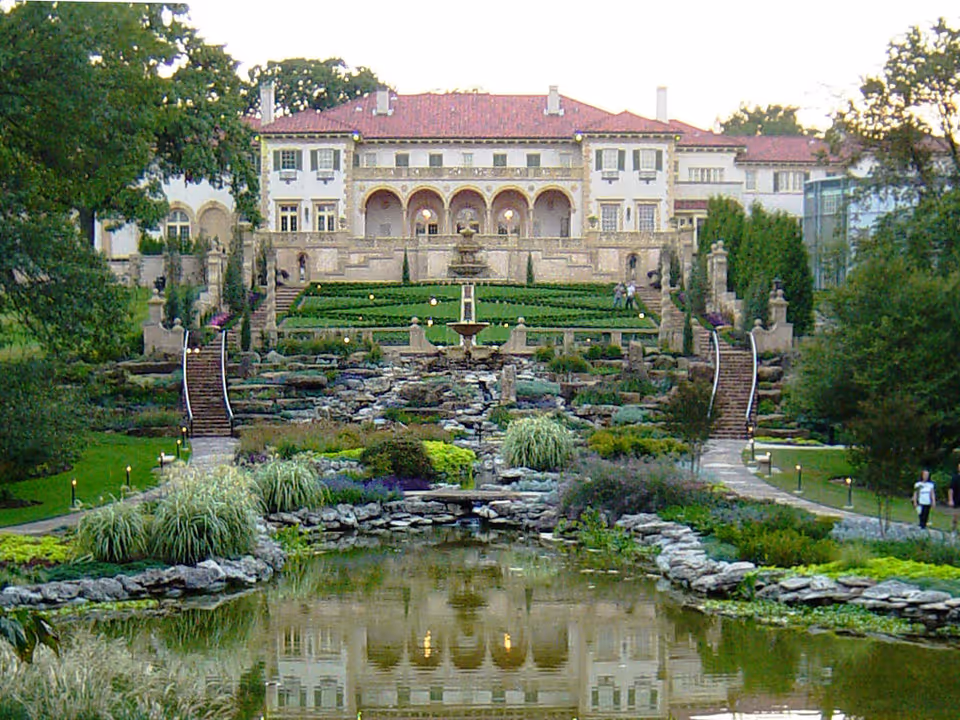 Exterior view of a grand estate with terraced gardens, fountain, and pond.