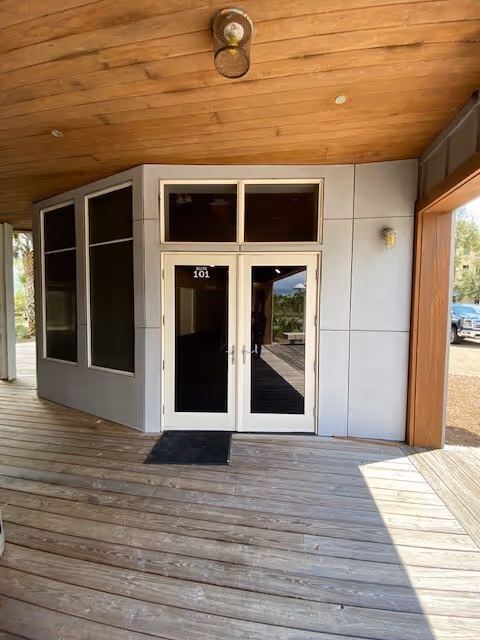Covered wooden entry with glass doors and a ramp to the building entrance.