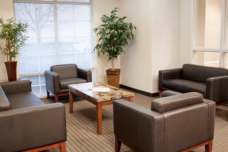 A modern lounge area with brown leather chairs, a marble coffee table, and plants.