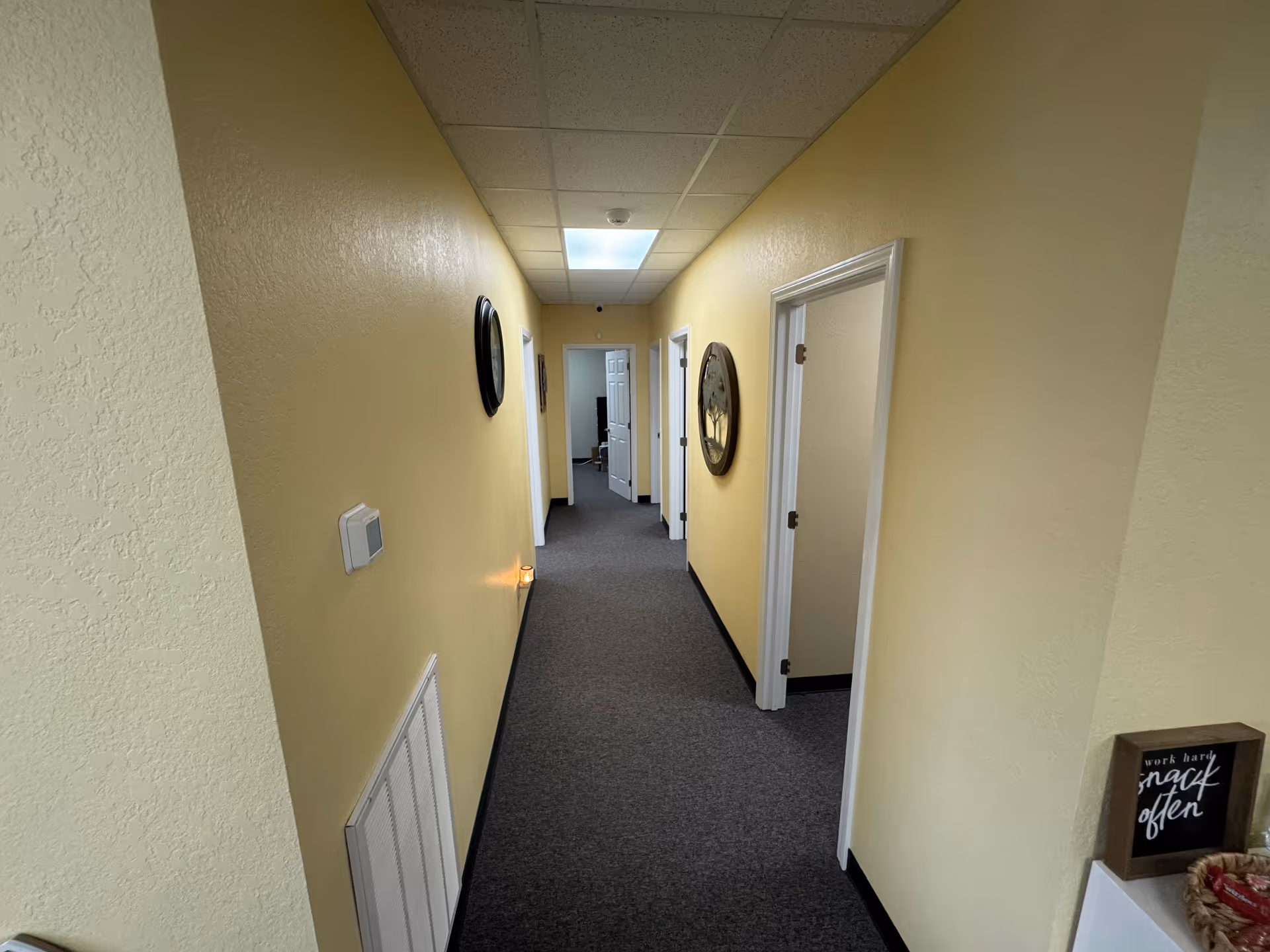 Long, yellow-walled hallway with closed doors and carpeted floor inside a senior living facility