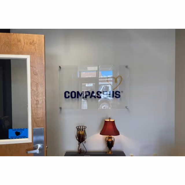 Compassus logo on glass plaque mounted on light gray interior wall