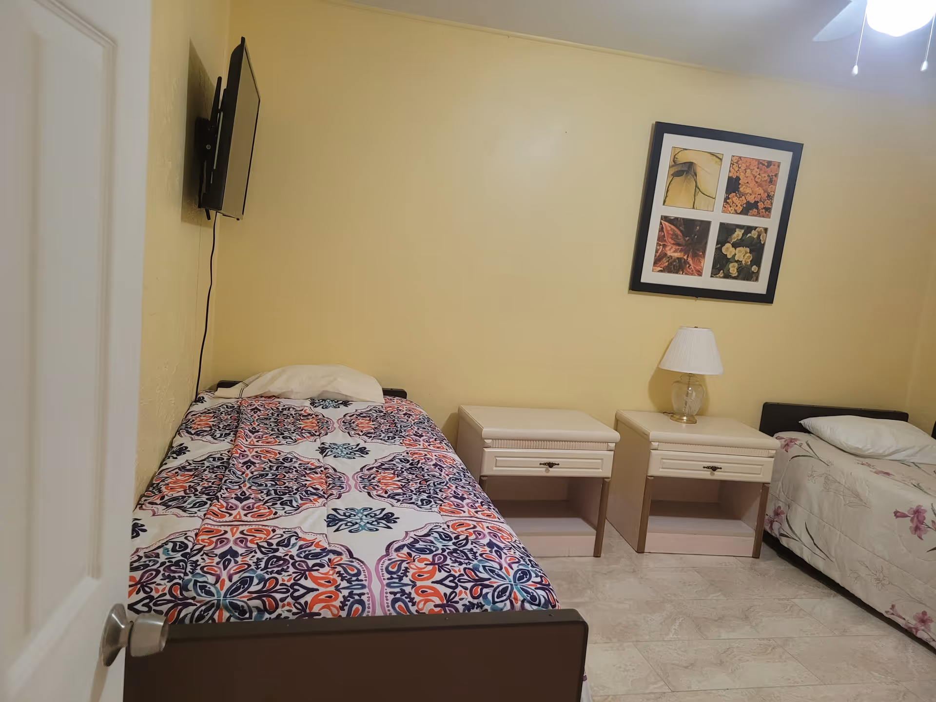 Two single beds with nightstands, a lamp, and wall art in a resident room.