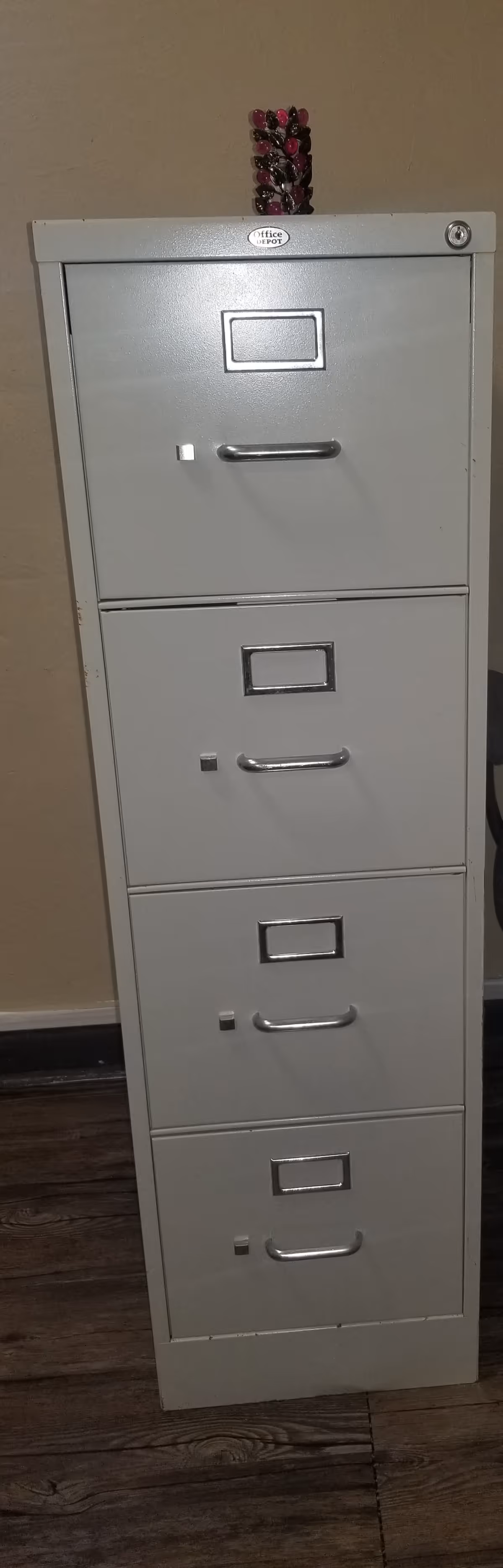 Tall grey metal filing cabinet with four drawers stands in a beige hallway.