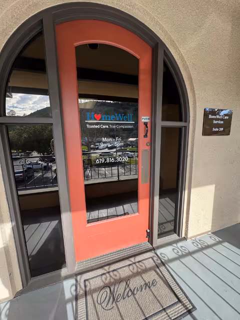 Red front door with glass panels and HomeWell Care Services logo at building entrance.