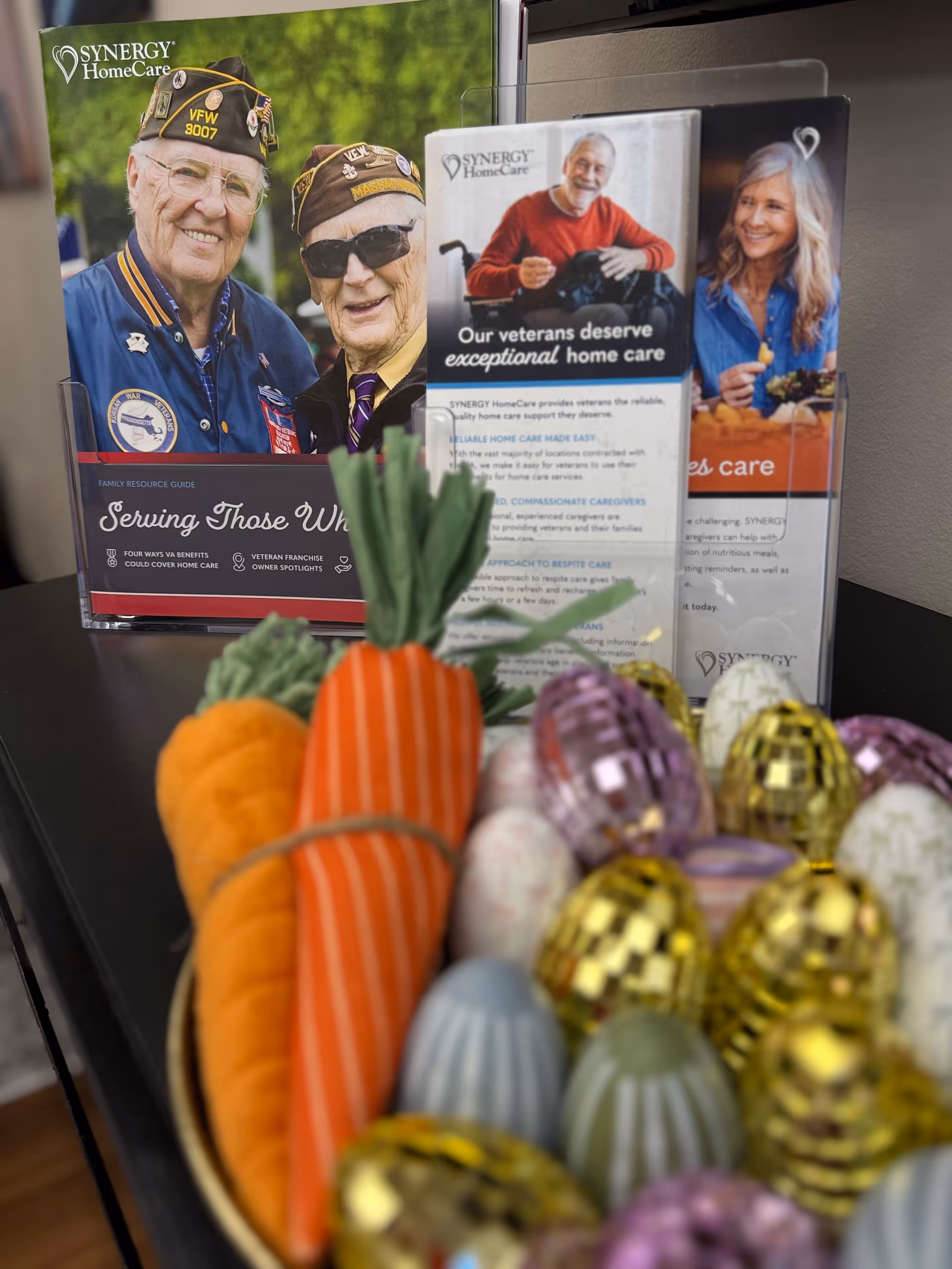 Promotional SYNERGY HomeCare brochures on a desk with carrots and decorative eggs.