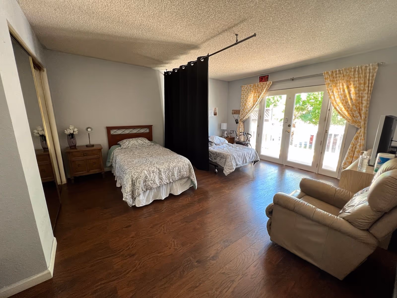 Two single beds separated by a black divider, dresser, sofa, and sliding glass doors.