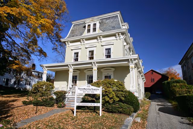 Front view of a cream-colored, multi-story building with a nursing registry sign and autumn trees.