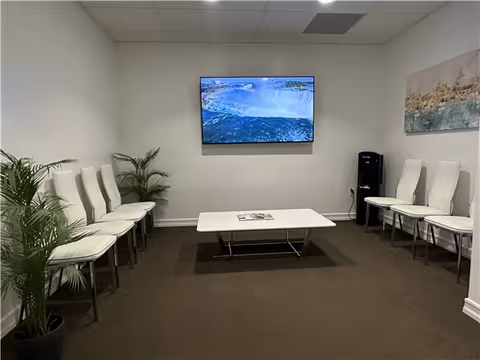 A waiting room with white chairs along the walls, a center coffee table, and a TV.
