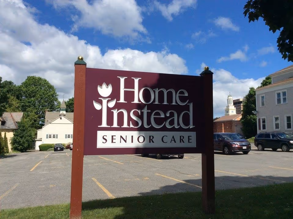 A large maroon Home Instead Senior Care sign in a parking lot under a blue sky.