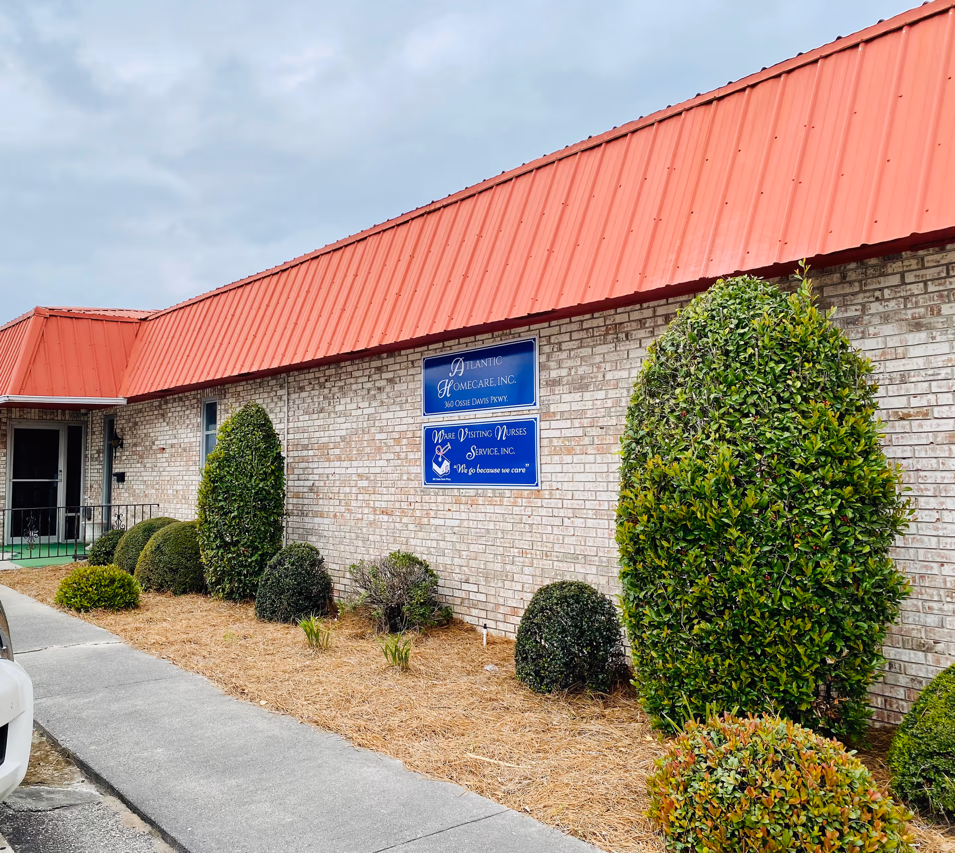 Exterior view of Adoration Home Health facility with brick walls, red metal roof, and landscaping.