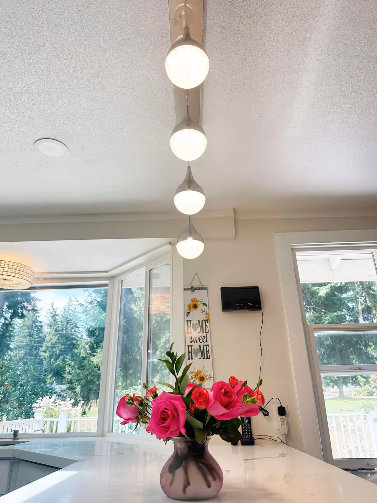 Bright kitchen area with a vase of pink roses on a white countertop near large windows.