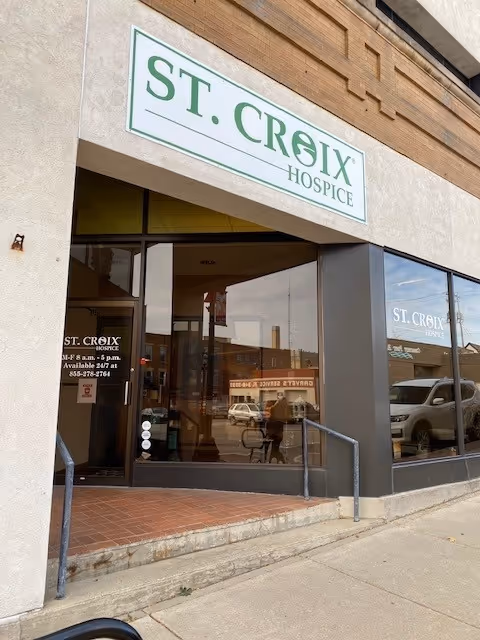 Exterior view of St. Croix Hospice storefront with glass doors and green sign.