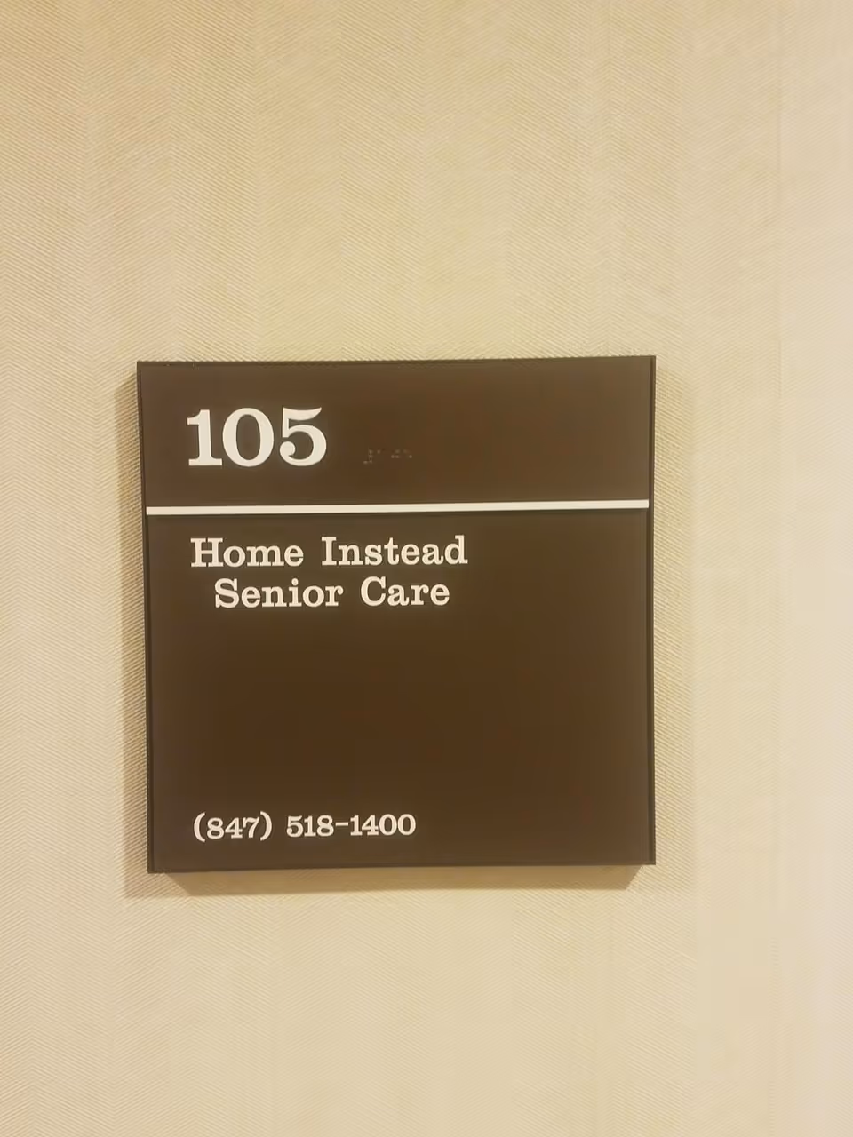 A brown sign on a beige wall reading 105, Home Instead Senior Care.