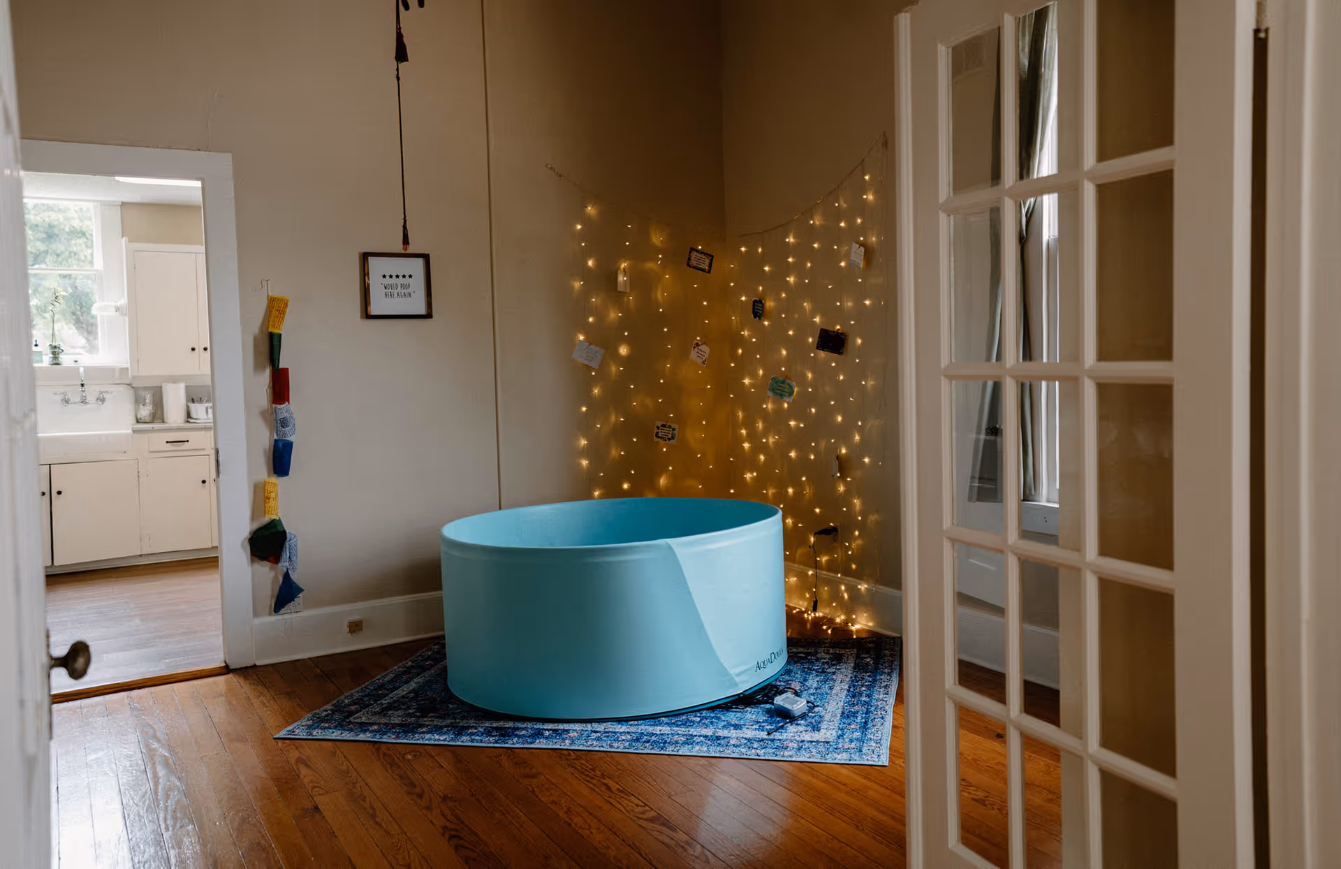 Bright teal birthing tub in a softly lit interior with string lights on a blue rug.