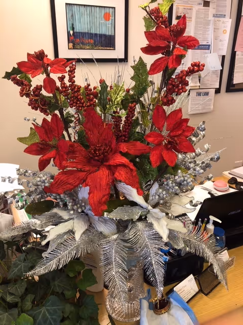 Large festive floral arrangement with red poinsettias and silver foliage on a cluttered office desk.
