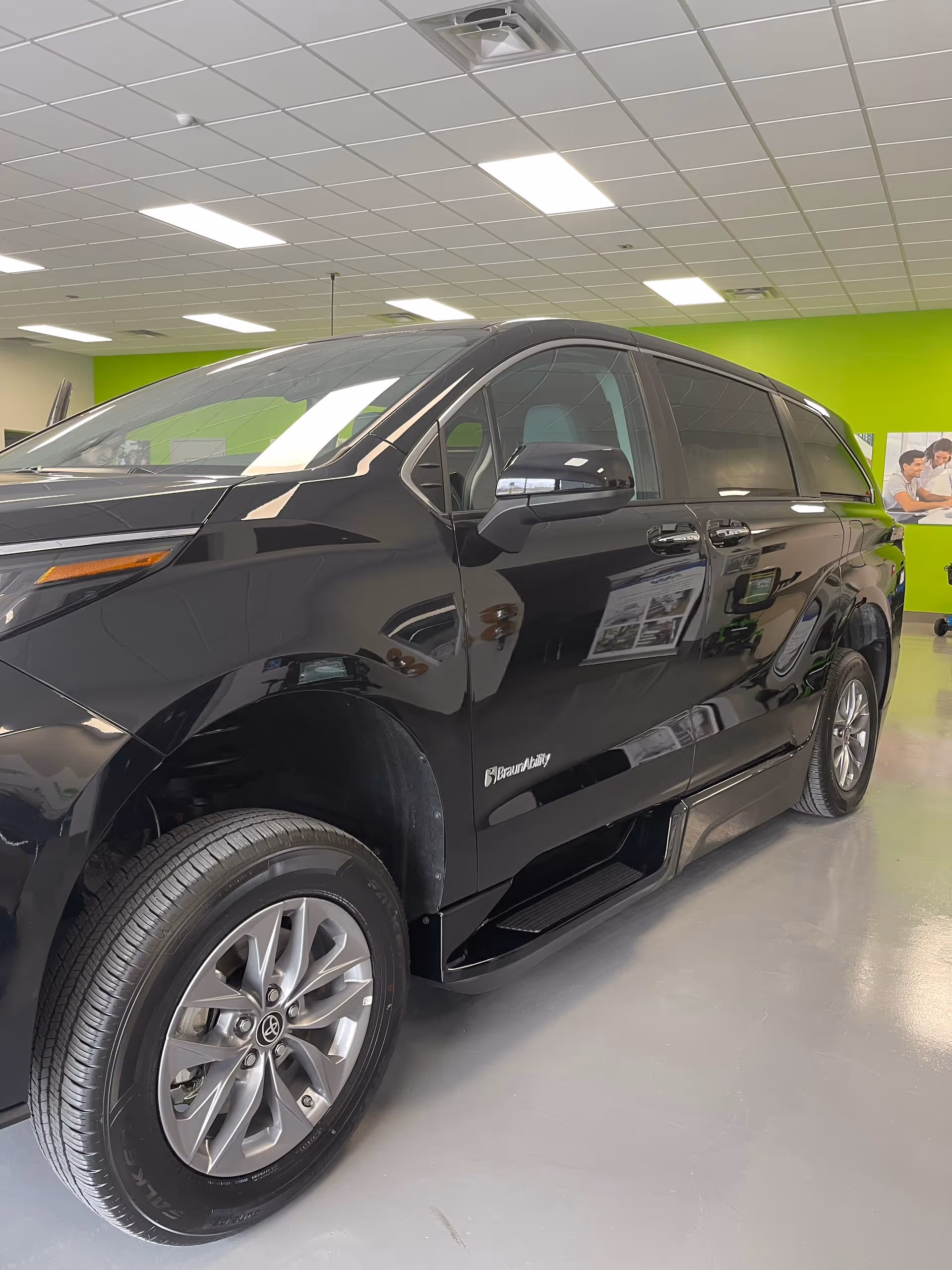 A black minivan is parked indoors in a bright MobilityWorks showroom.
