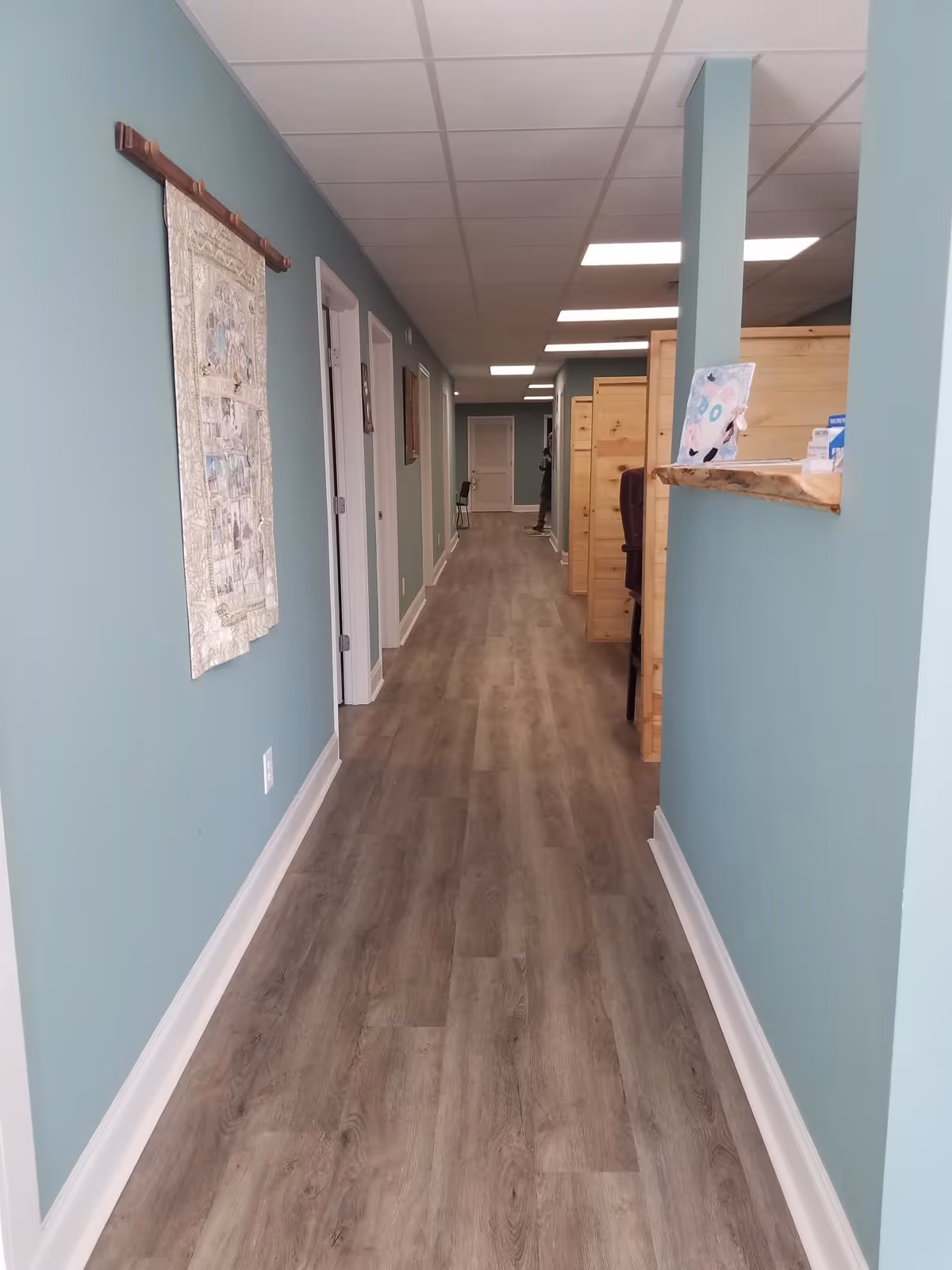 Long teal hallway in a senior living facility with doors and a reception counter.