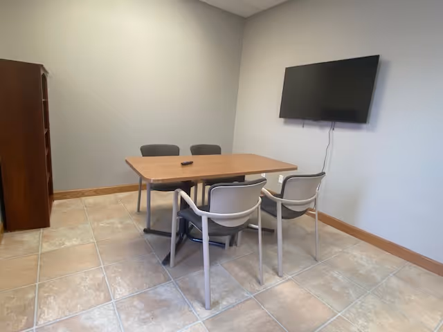 A small neutral-colored meeting room in Robland Home Health Care with table, four chairs, wall-mounted TV.