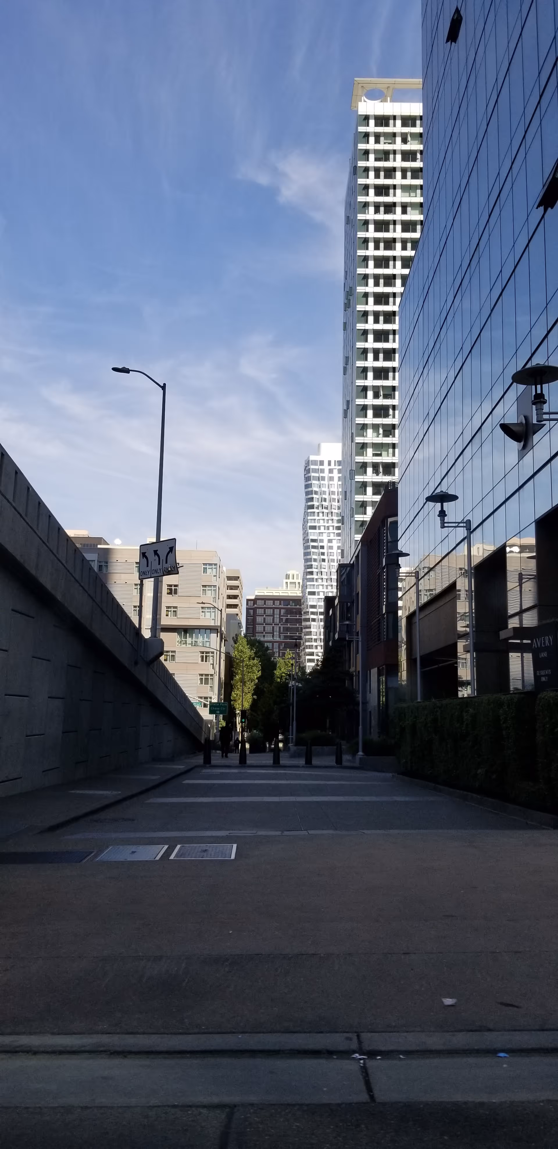 Urban city street lined with tall glass buildings under a blue sky.