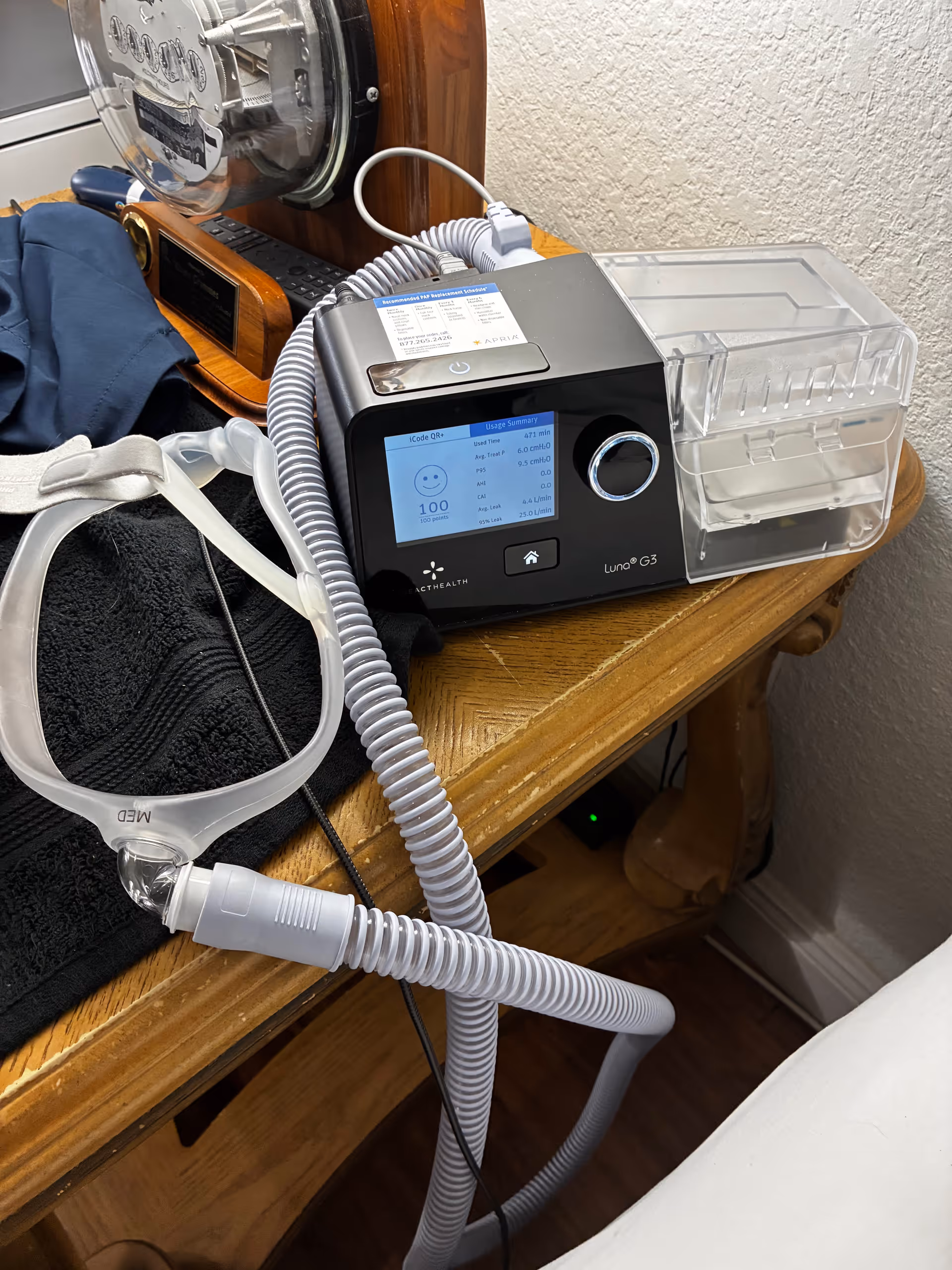 CPAP machine with mask and tubing sits on a wooden bedside table in a bedroom.