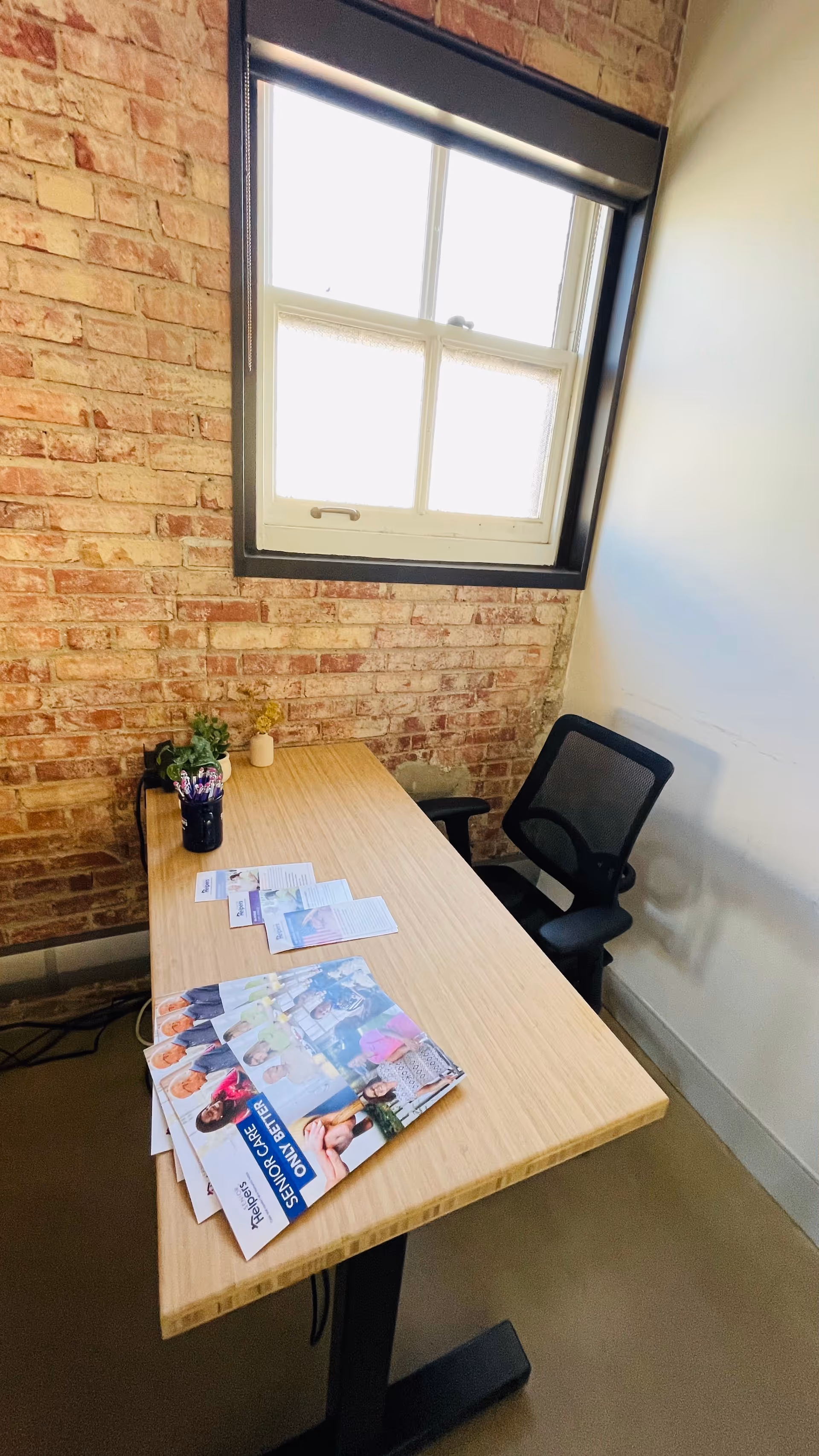 Office desk with brochures and a chair against a brick-walled interior.