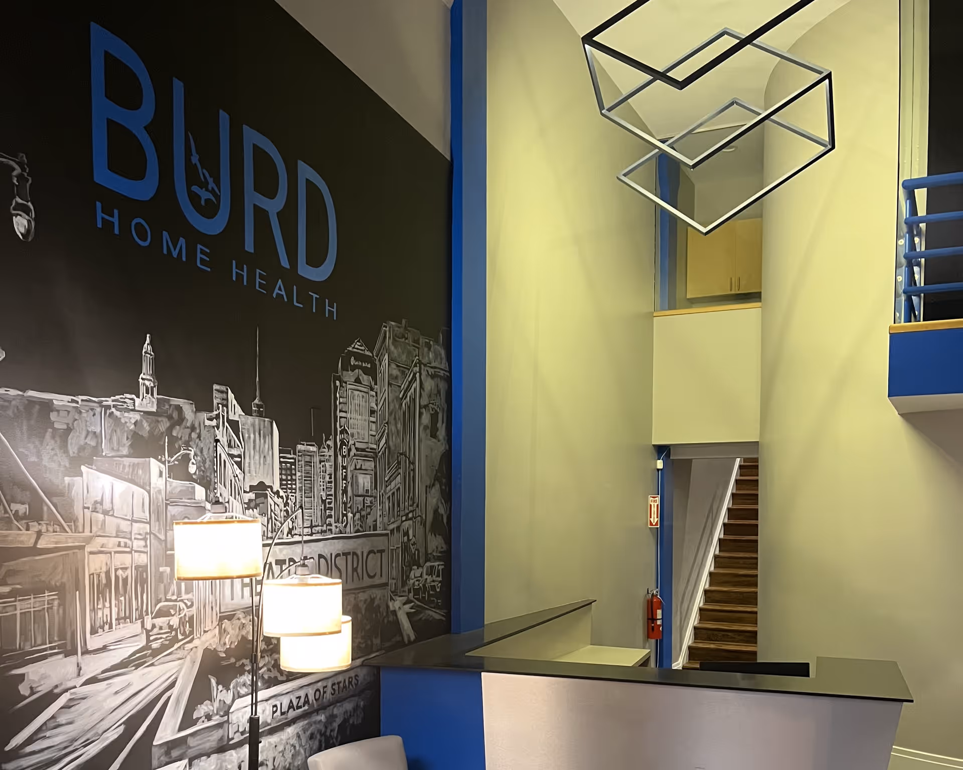 Modern reception area featuring Burd Home Health mural, blue accents, and a staircase.