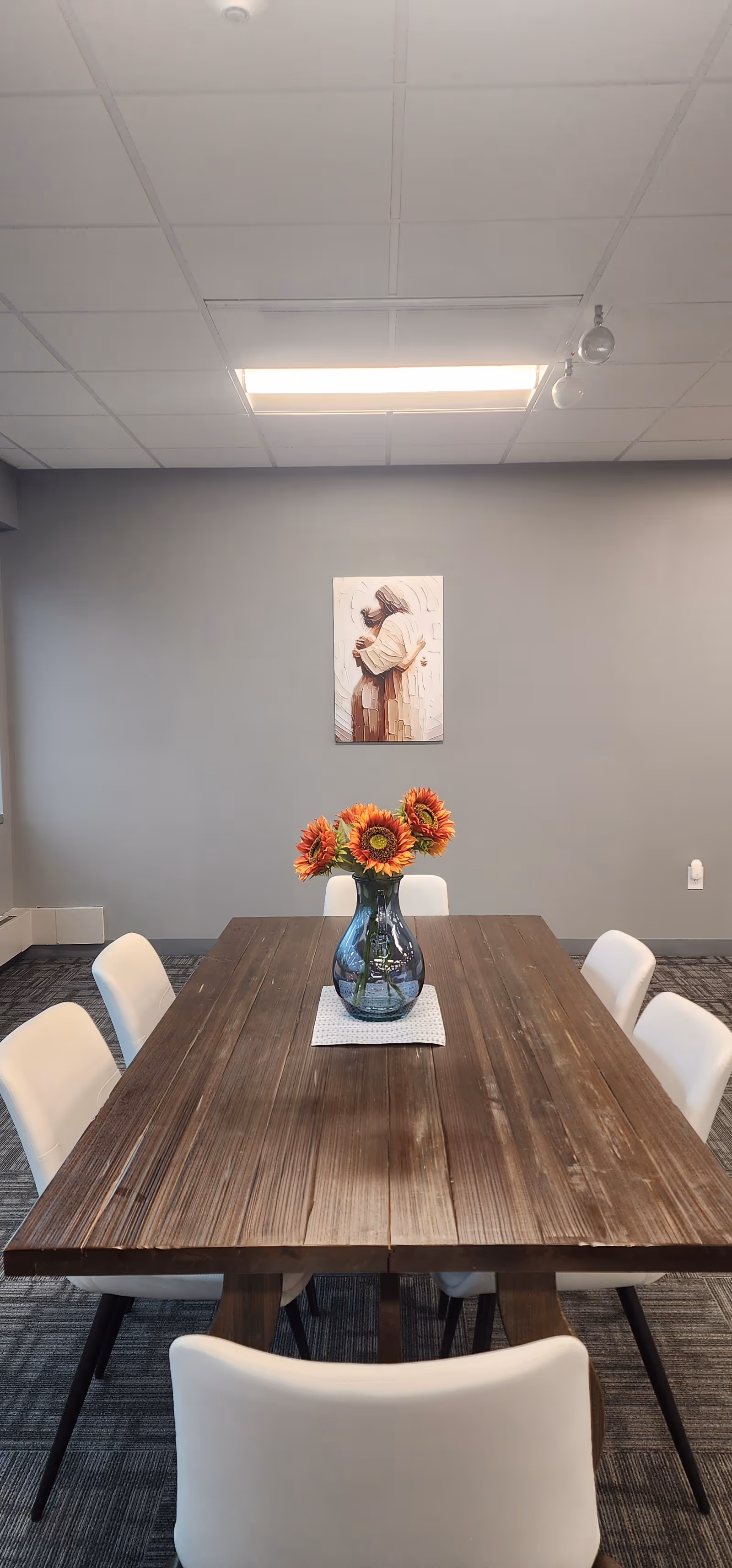 A wooden dining table with white chairs, a vase of sunflowers, and wall art.