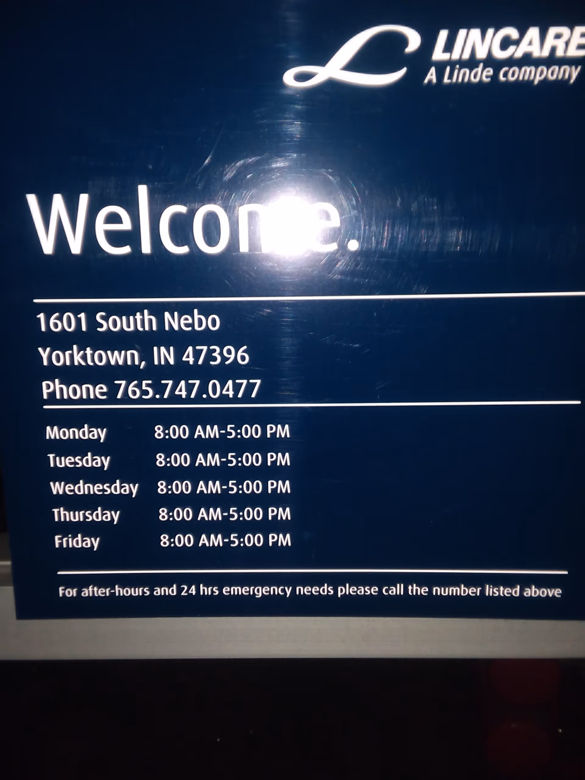 Dark blue sign displays Lincare logo, Welcome text, address, and business hours indoors.
