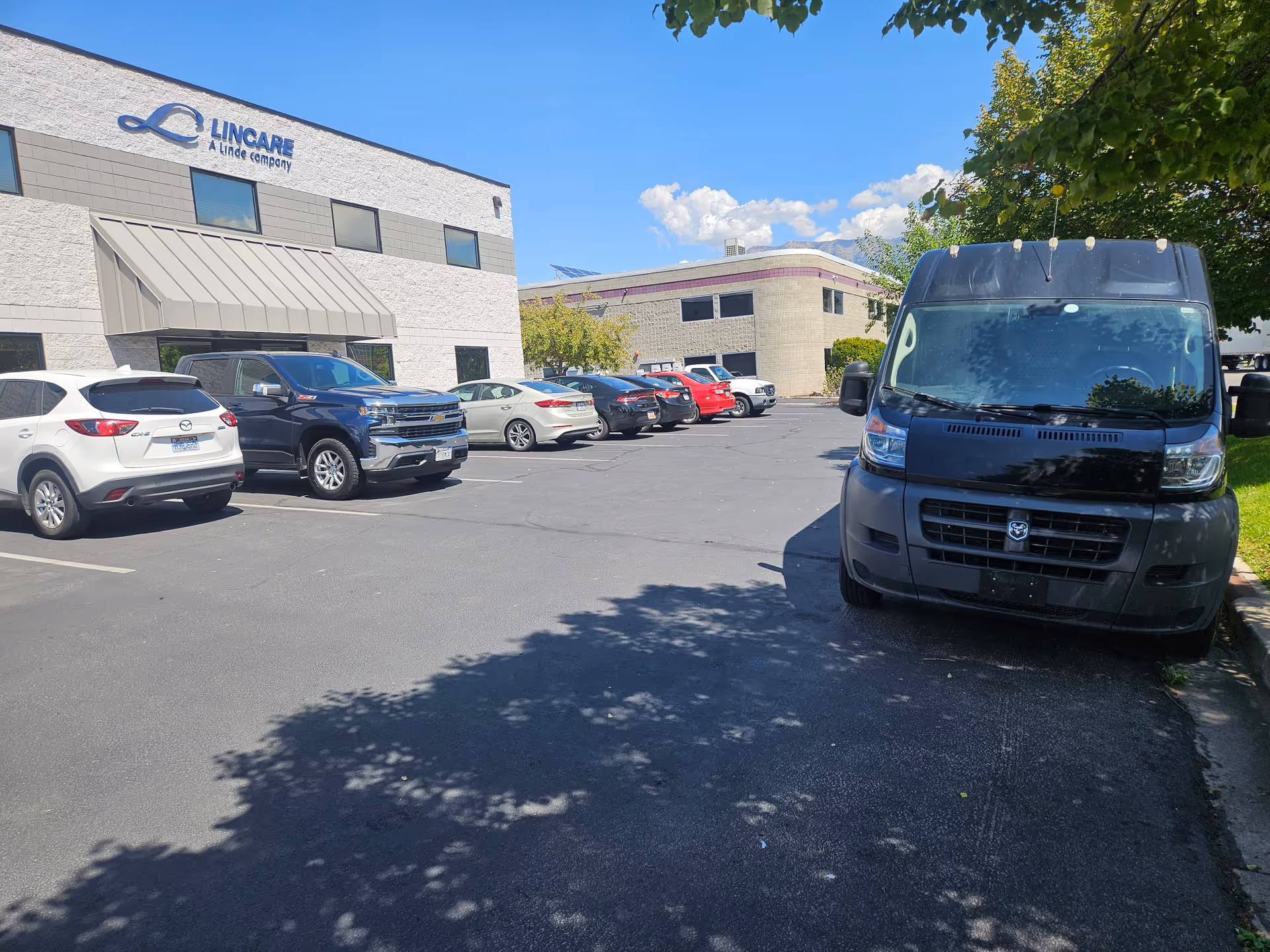 Front view of a LINCARE facility with a row of parked cars in a sunny lot.