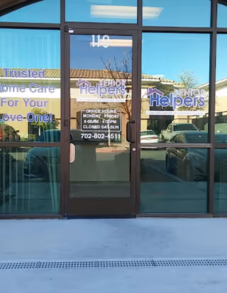 Glass storefront of Senior Helpers with doors, signage, and reflections of parked cars.