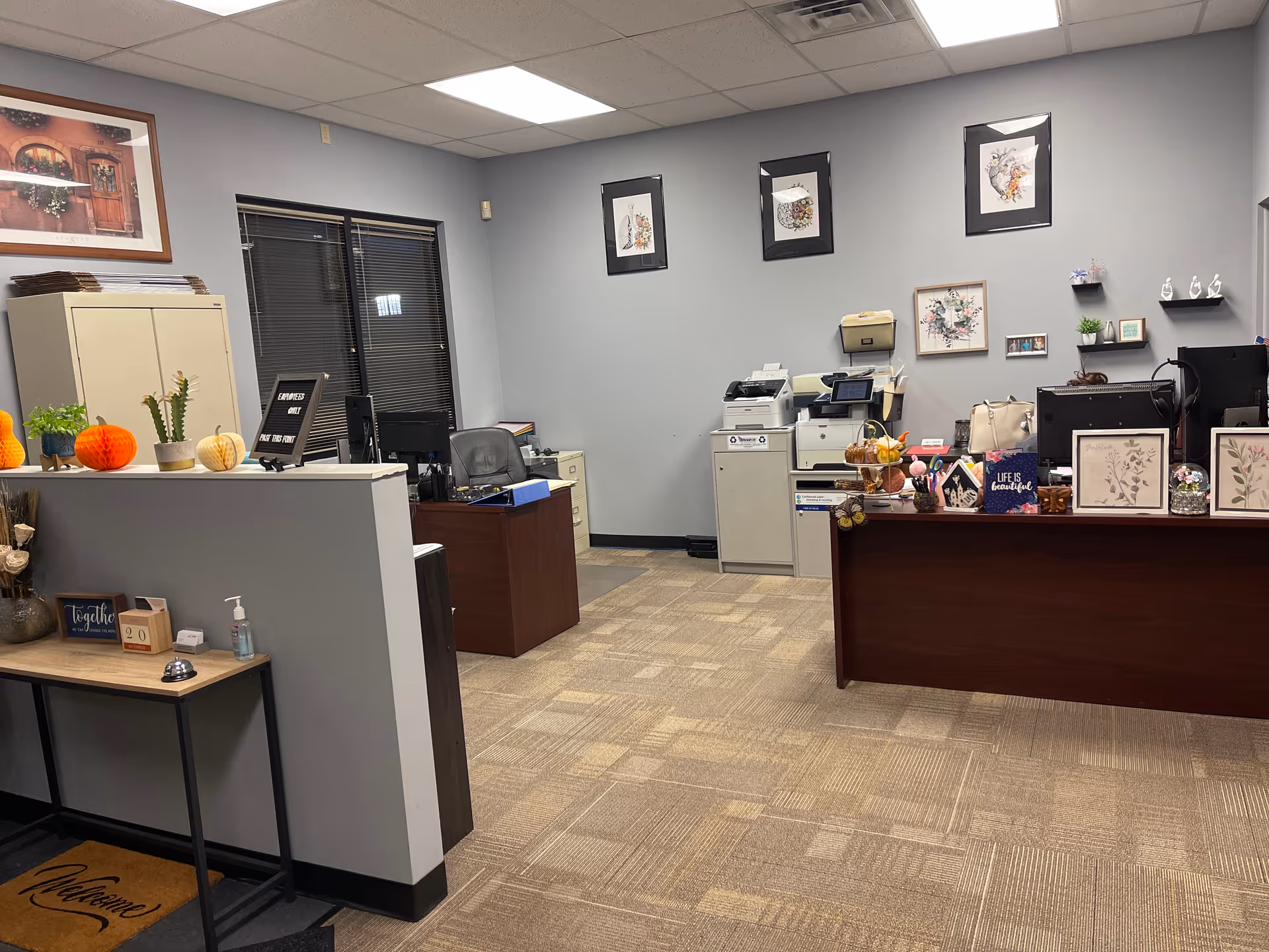 LINCARE reception area with desks, printers, framed art, plants, and pumpkins.