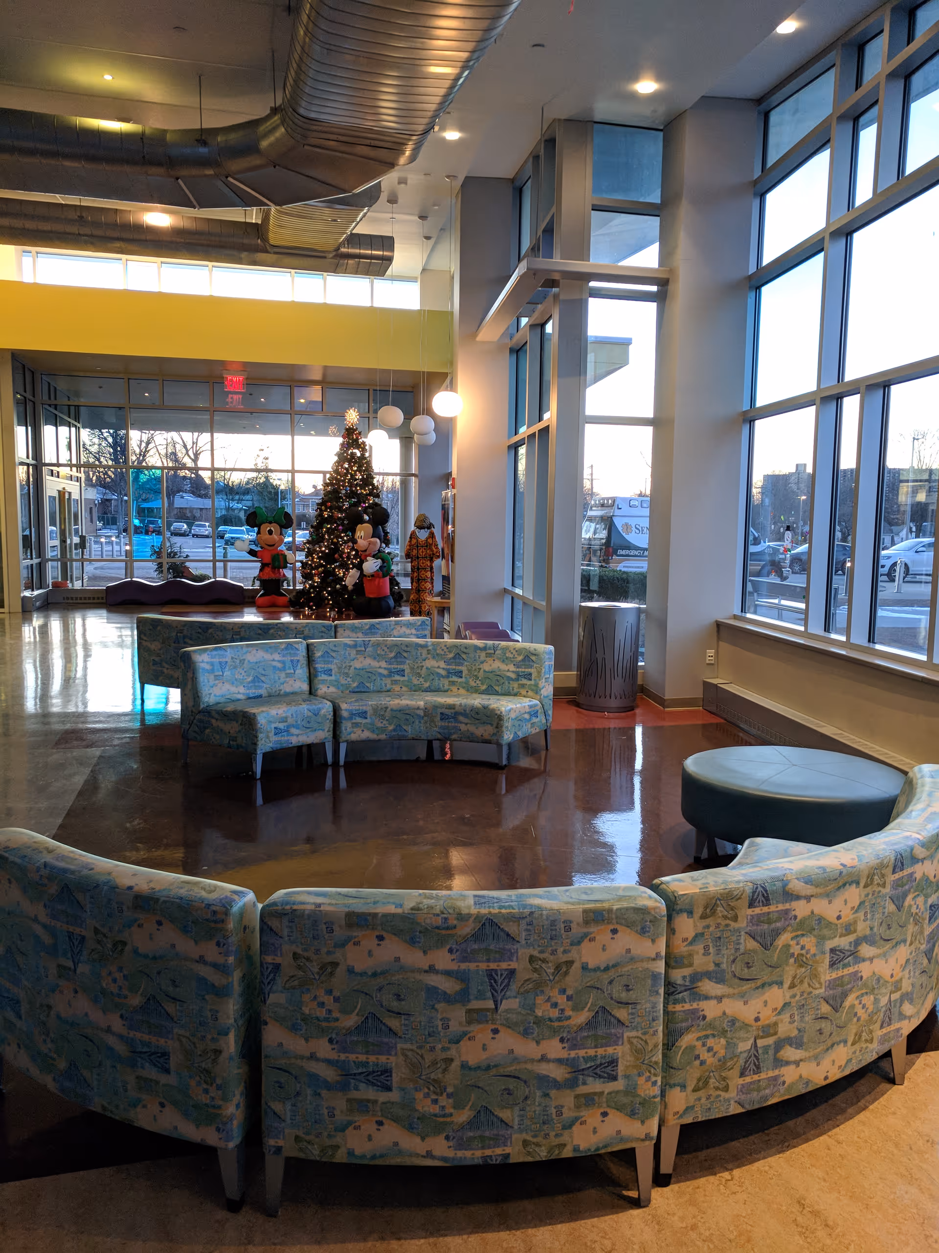 Bright modern hospital lobby with curved blue seating, large windows, and a Christmas tree.