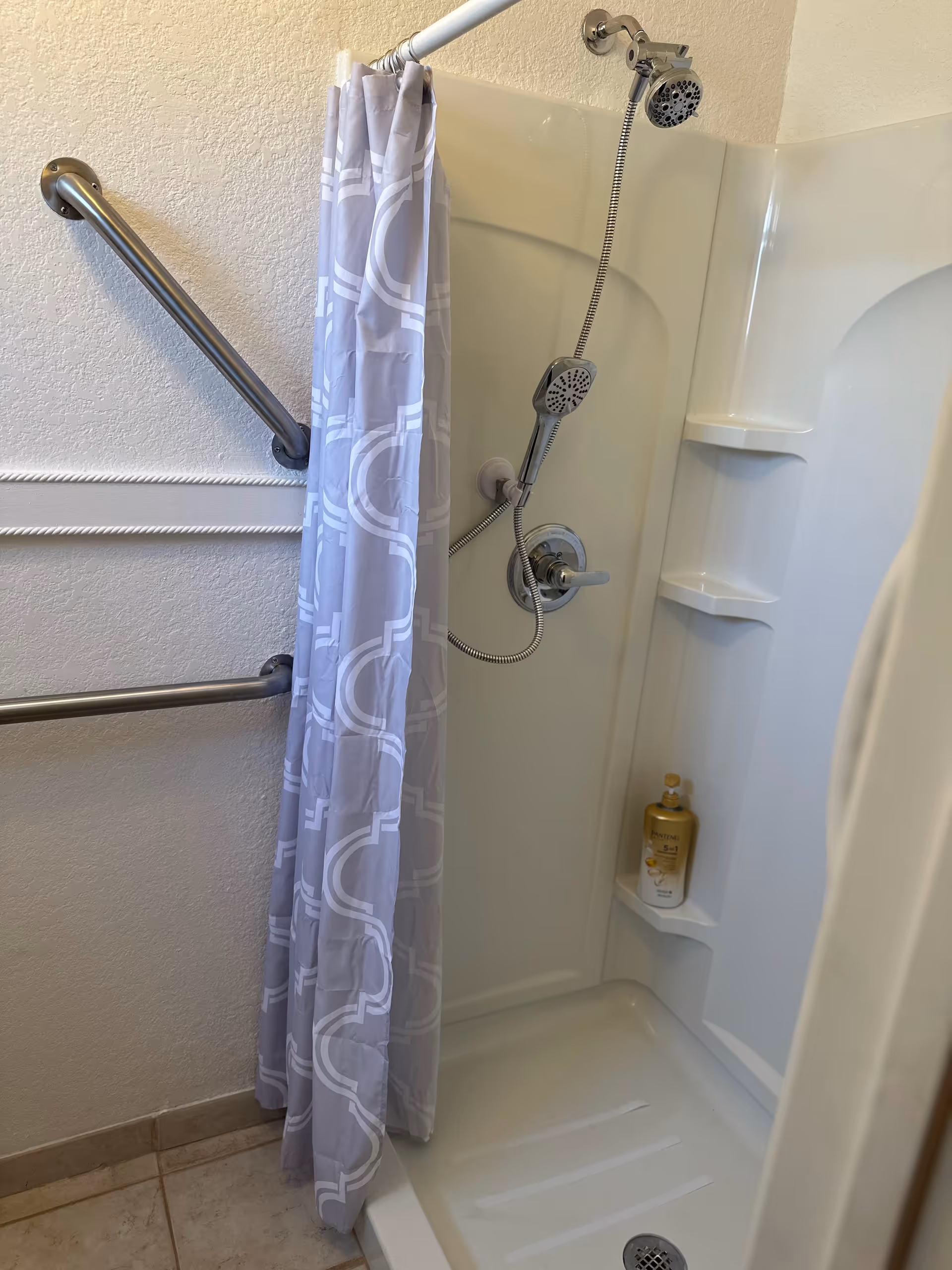 Accessible shower with grab bars, handheld showerhead, and shampoo shelf.