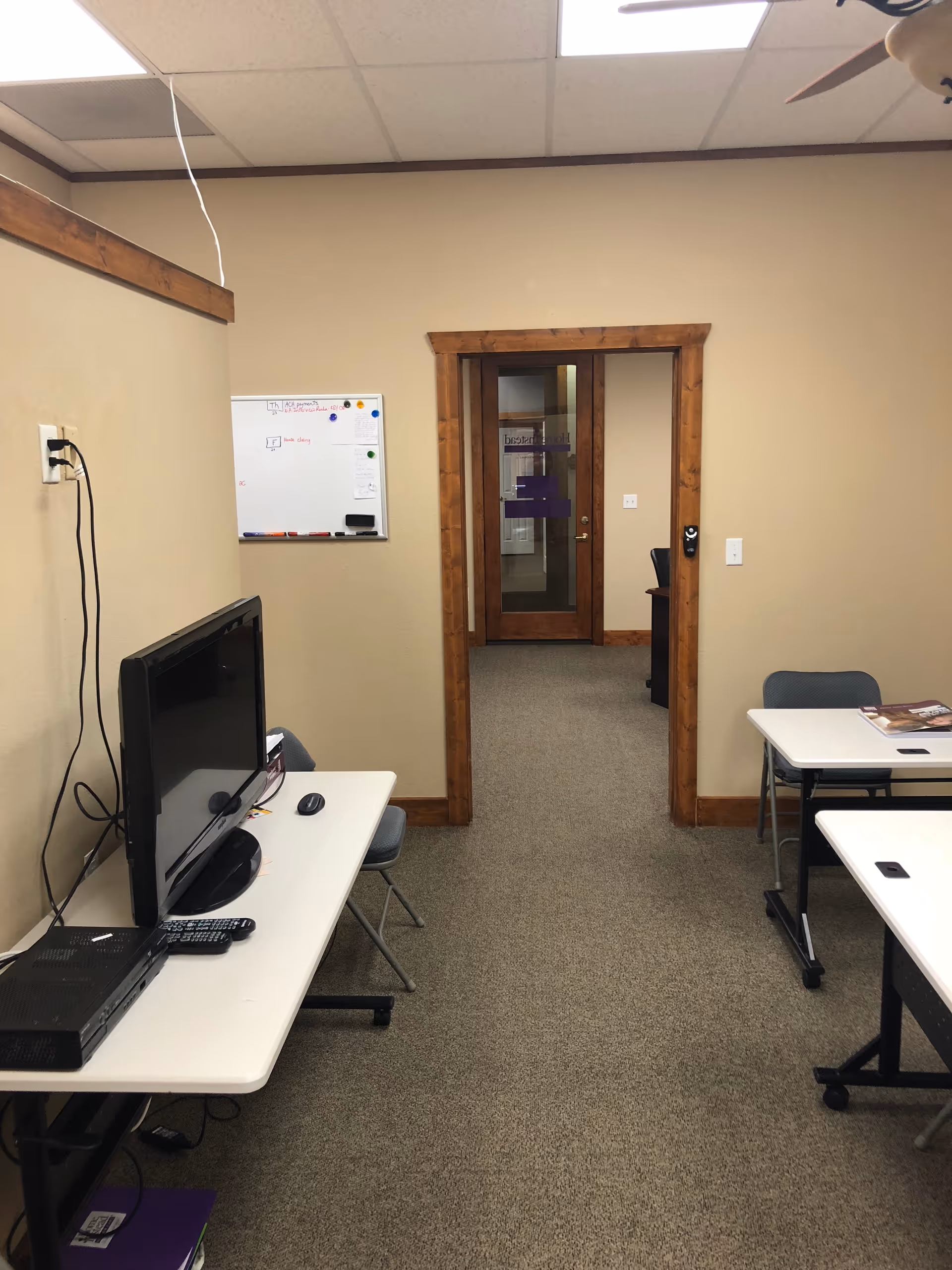 An interior office area with a computer desk, whiteboard, and doorway framed by wood trim.