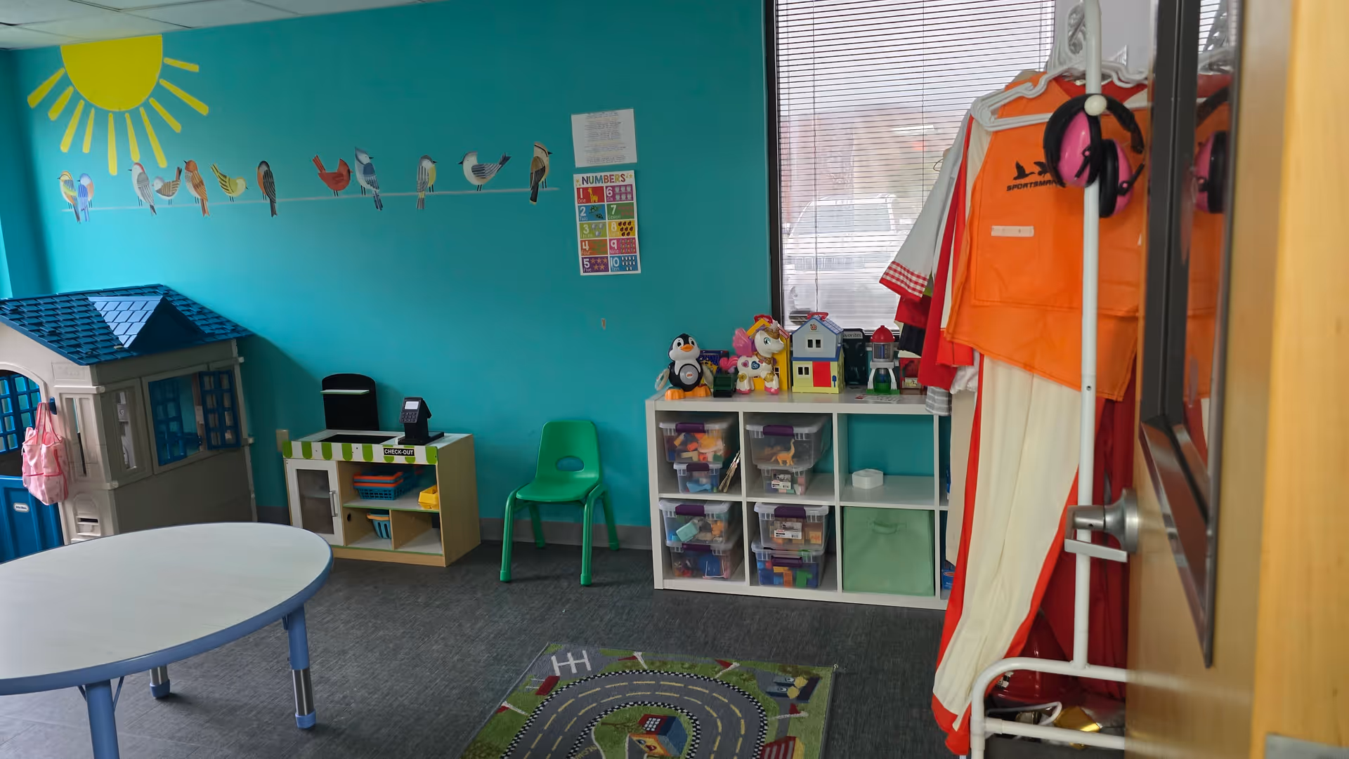Bright teal wall with sun mural, children's play area, and organized toy storage.