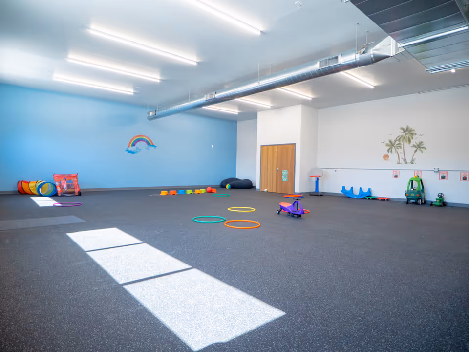 Bright indoor playroom with blue wall, rainbow mural, and colorful kid-sized equipment.