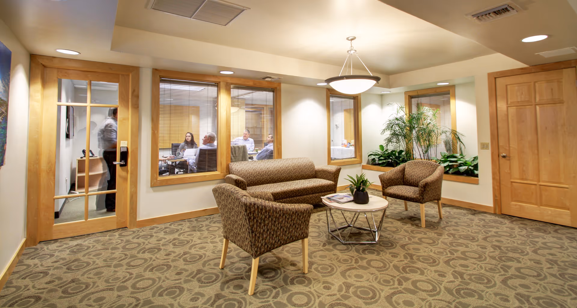 Cozy lounge area with brown patterned chairs, a glass coffee table, and indoor plants.