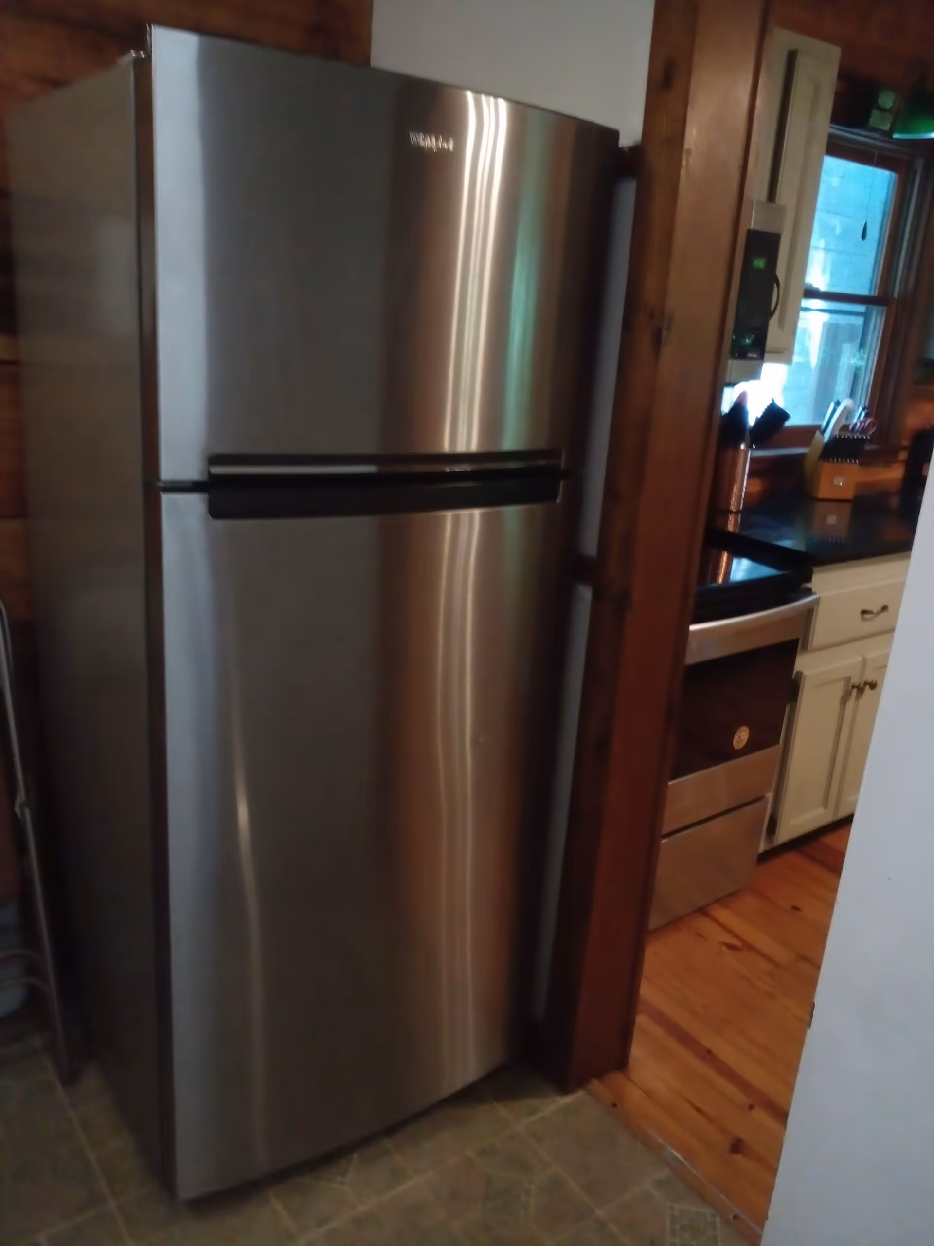 Stainless steel refrigerator in a kitchen with wooden trim and white cabinets