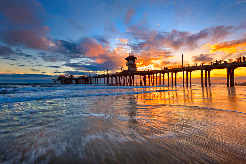 Sunset over a long pier extending into the ocean with glowing reflections.