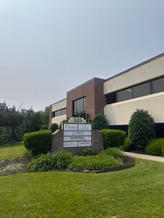 Exterior view of BAYADA Assistive Care facility with sign, brick and beige building, green lawn.