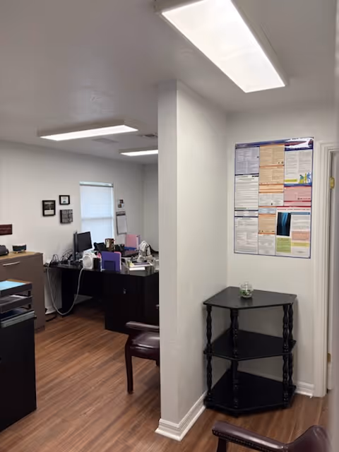 Office area inside Angels Home Care with desks, computers, and a shelf beside a bulletin board.
