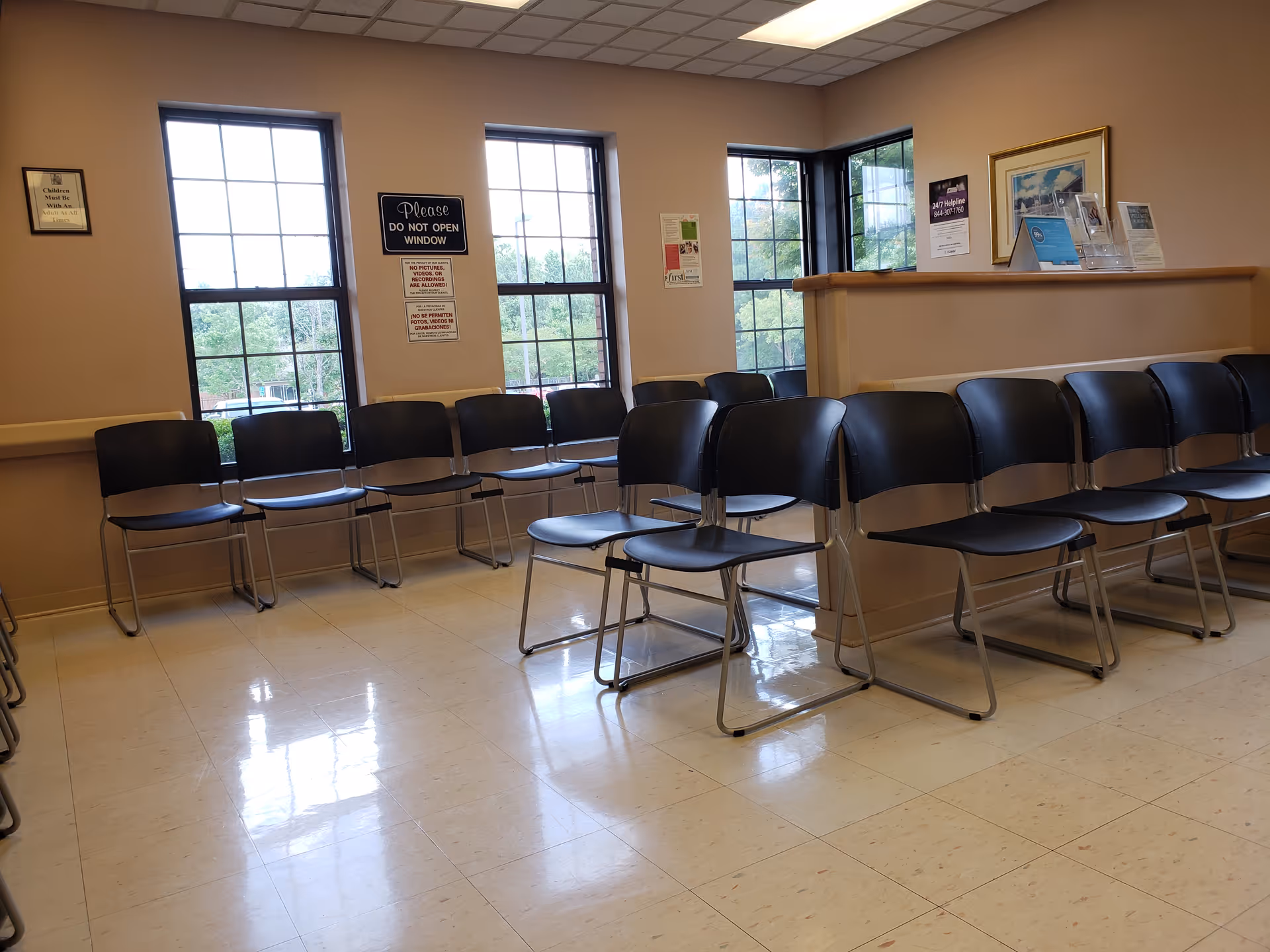 Row of black chairs in a waiting area by large windows and reception desk.