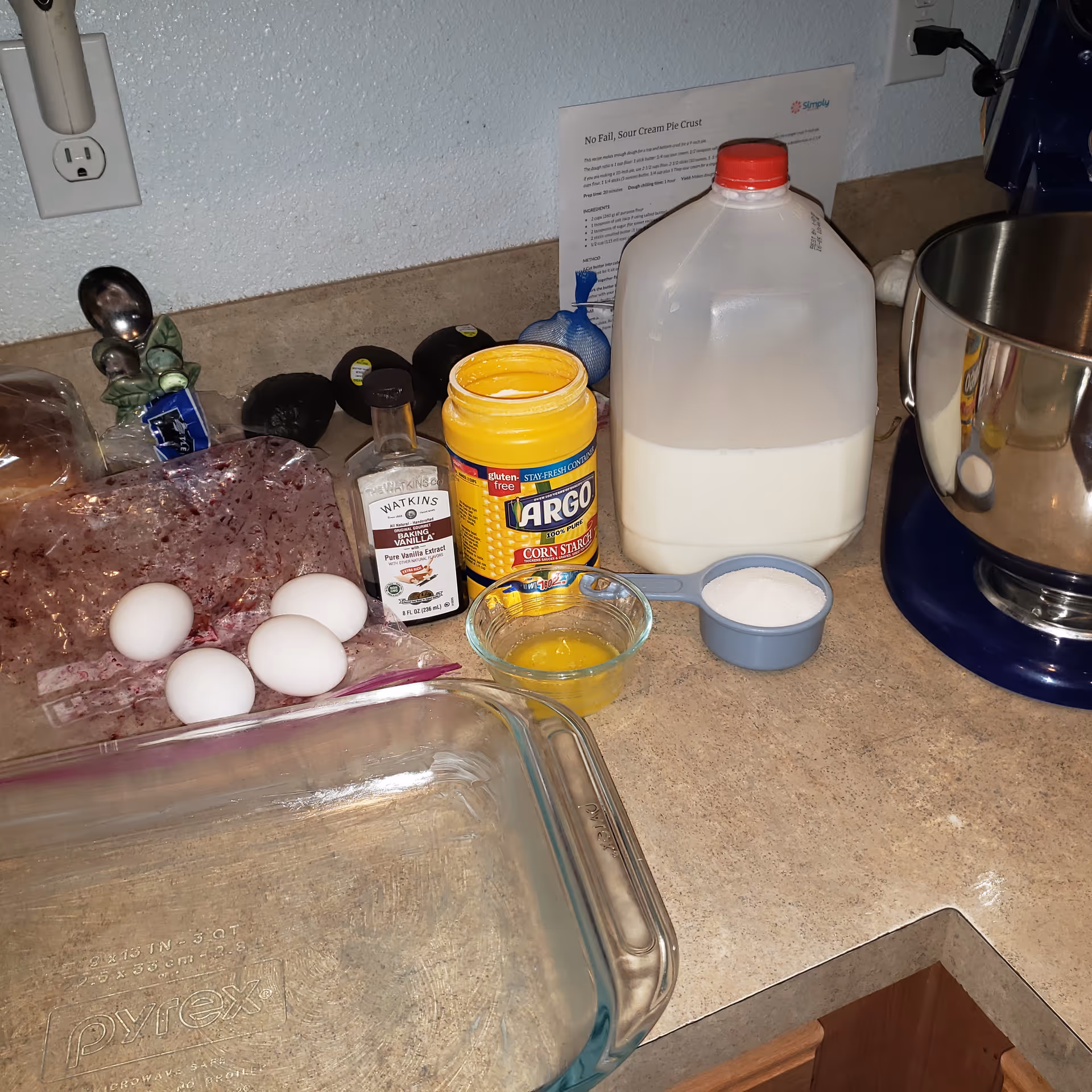 Countertop kitchen scene with eggs, vanilla, Argo cornstarch, milk jug, and a stand mixer.