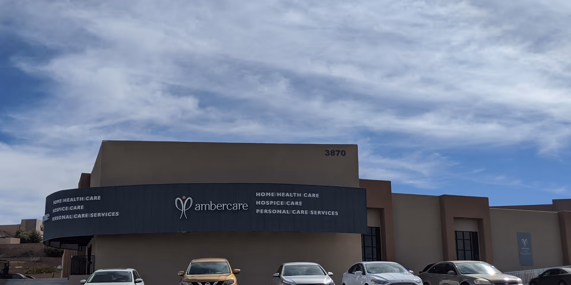 Ambercare building front with curved sign, beige exterior, and several parked cars.