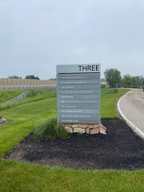 Outdoor sign with 'THREE' directory and surrounding landscaping beside a curved road.