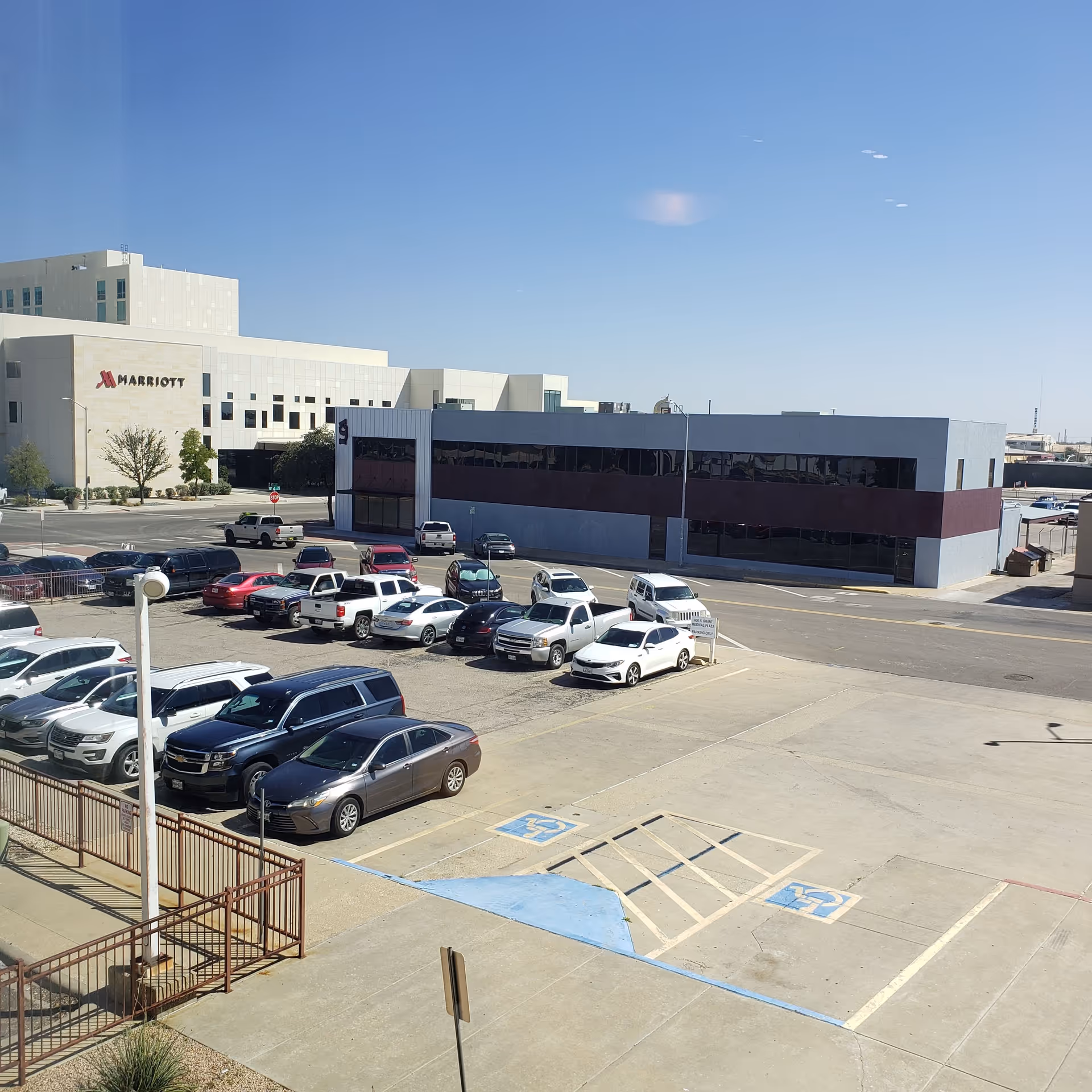 Exterior view of a Marriott hotel and adjoining building with a parking lot.