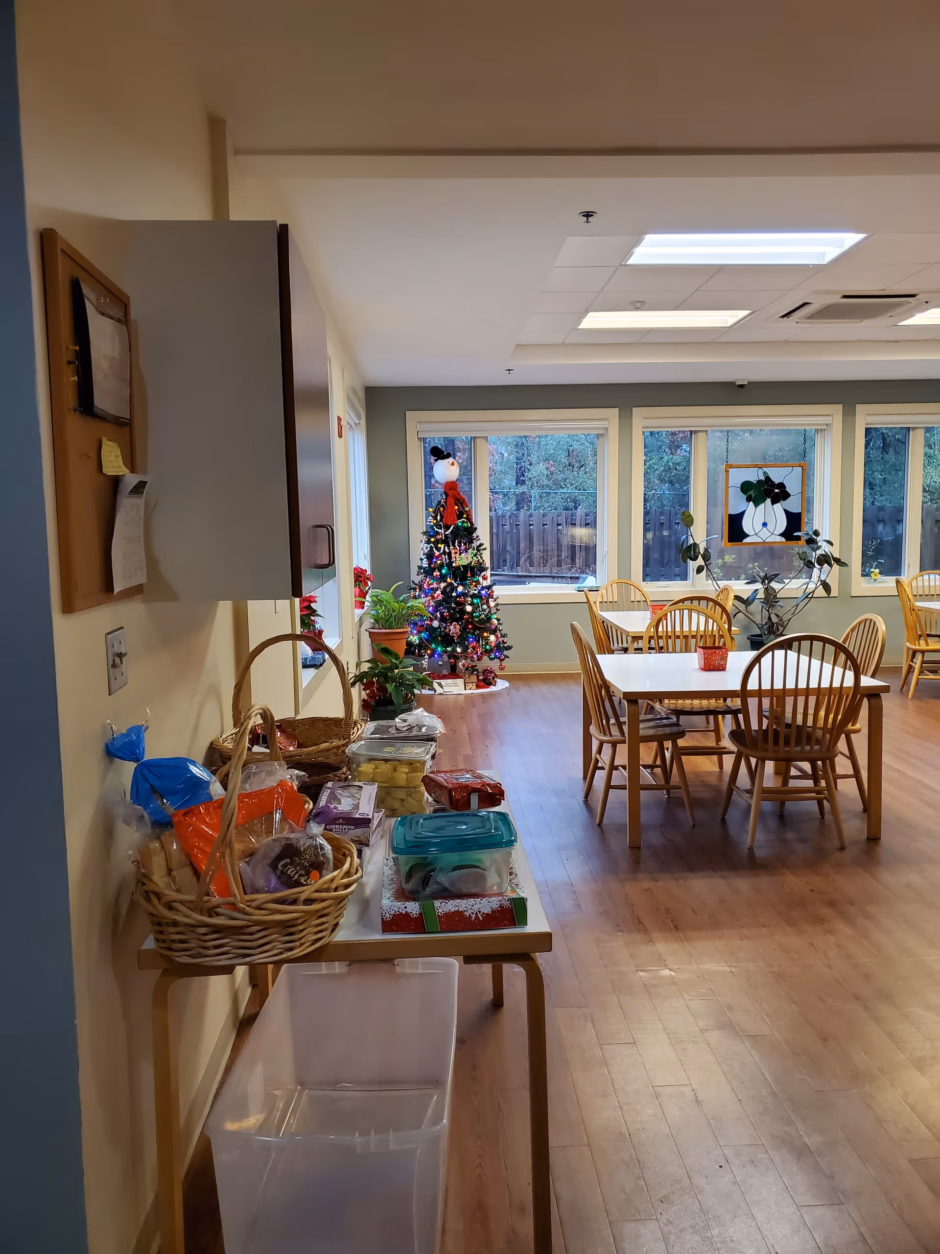 Interior dining area with wooden tables, chairs, a Christmas tree, and baskets on a side table.