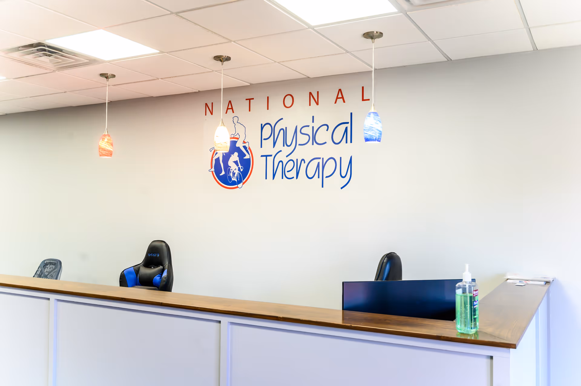 Reception area with a front desk, chairs, and a National Physical Therapy logo on the wall.