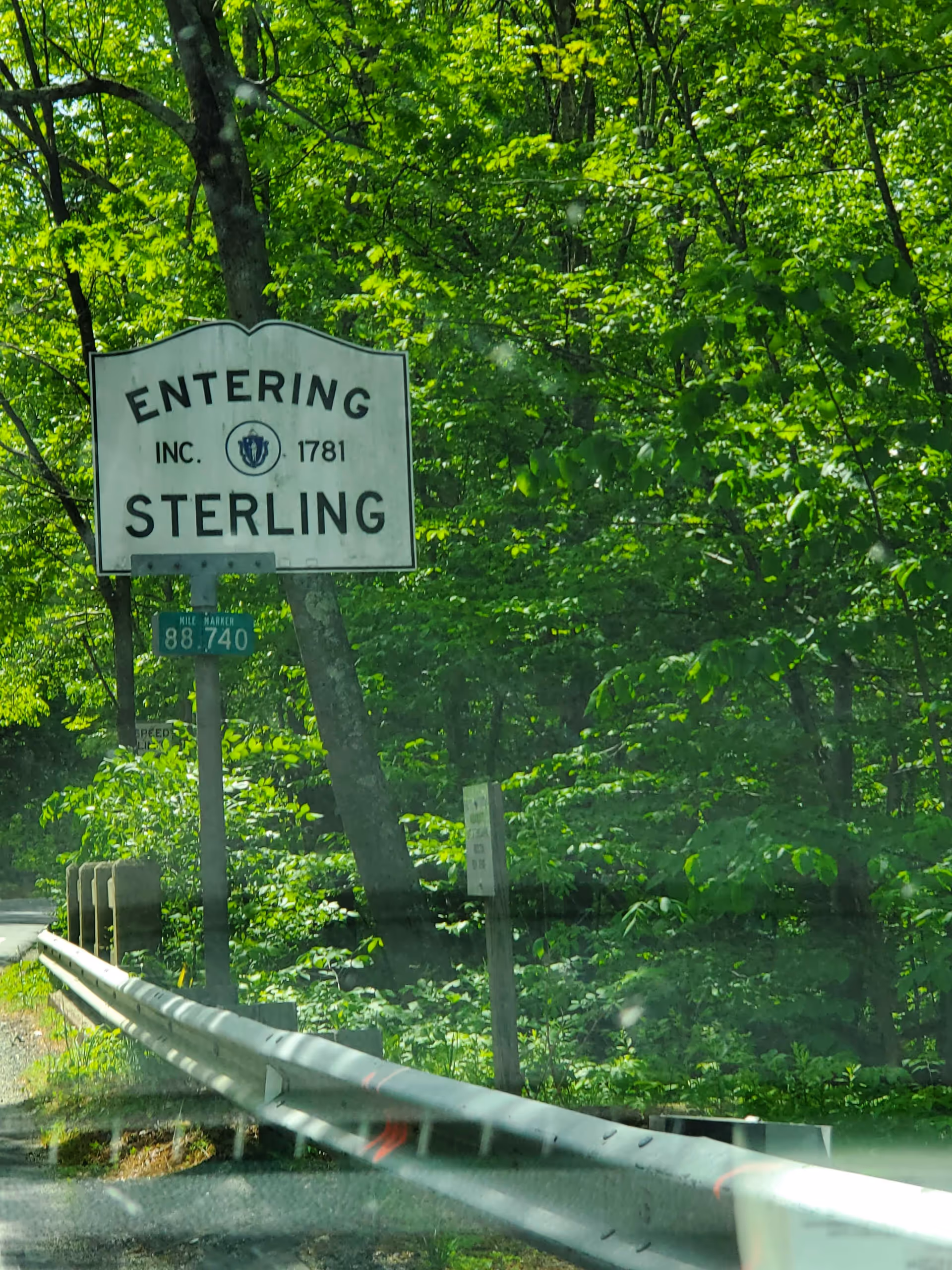 Green wooded roadside with an 'Entering Sterling' sign beside a guardrail.