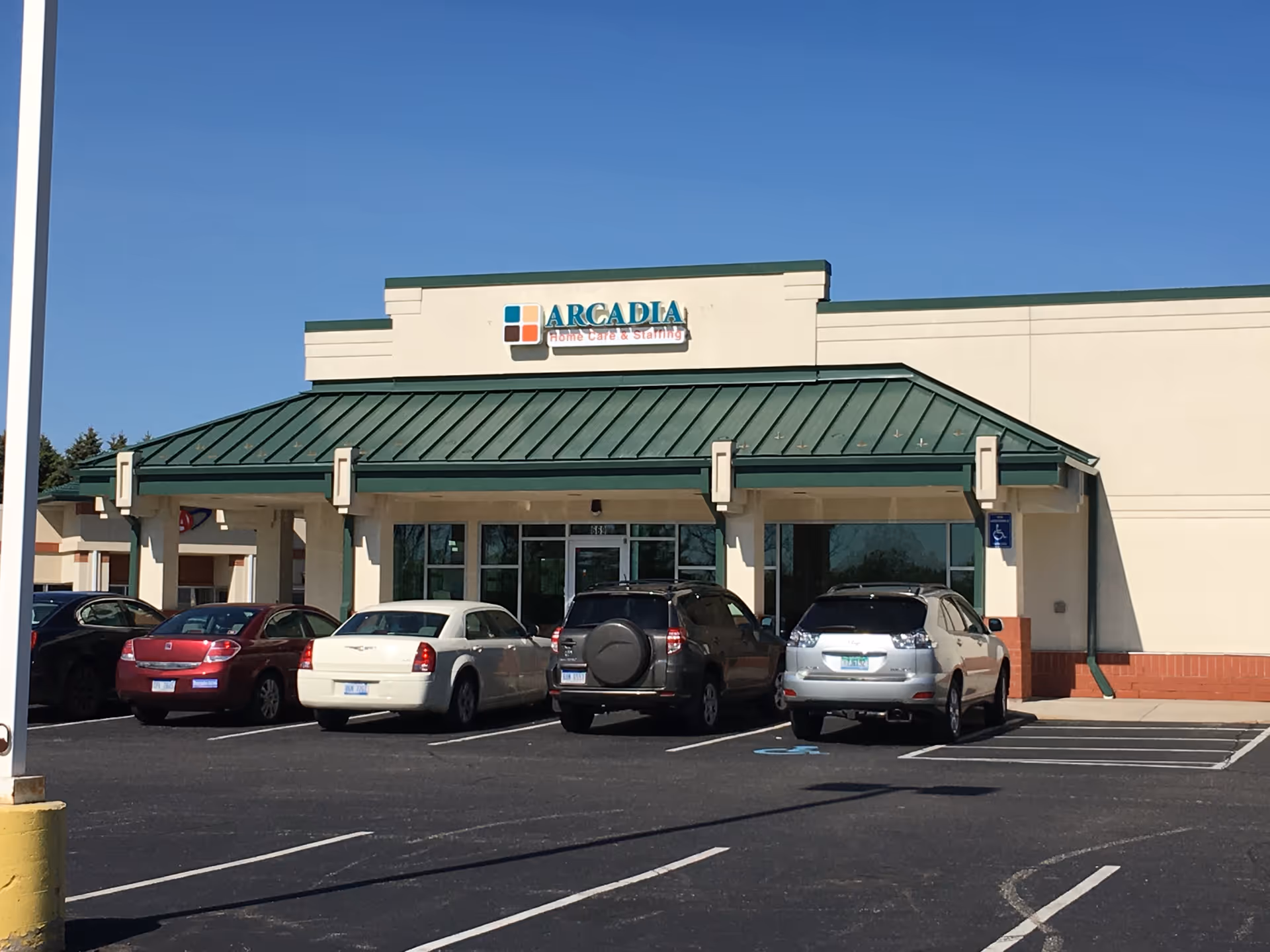 Front view of Arcadia Home Care & Staffing building with a metal roof and parked cars.